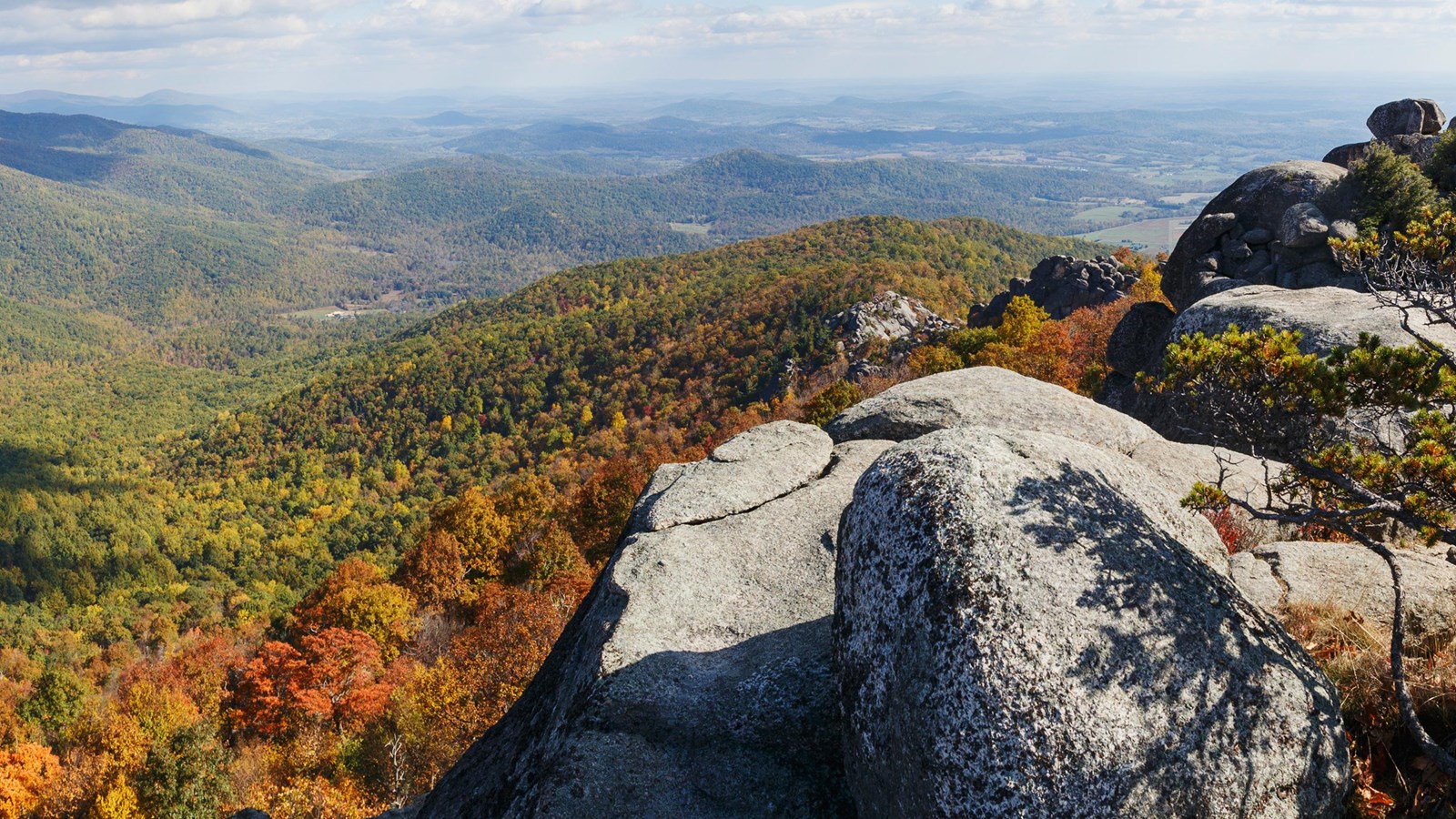 A rock outcrop overlooks mountain layers below, exploding with fall colors: red, orange, and yellow