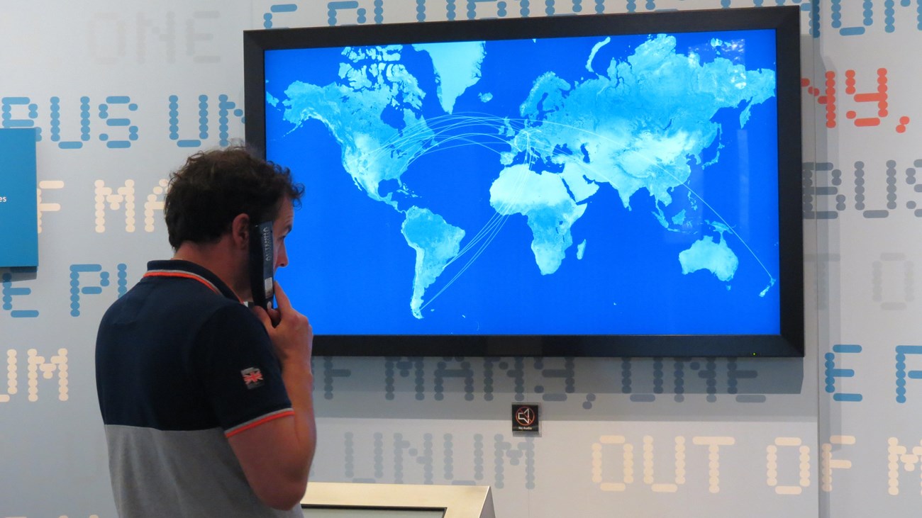 Man listening to audio tour while watching a display panel of the continents.
