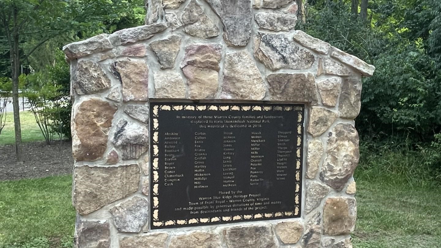 A stone chimney bearing a dark metal plaque stands at the edge of a red brick patio.