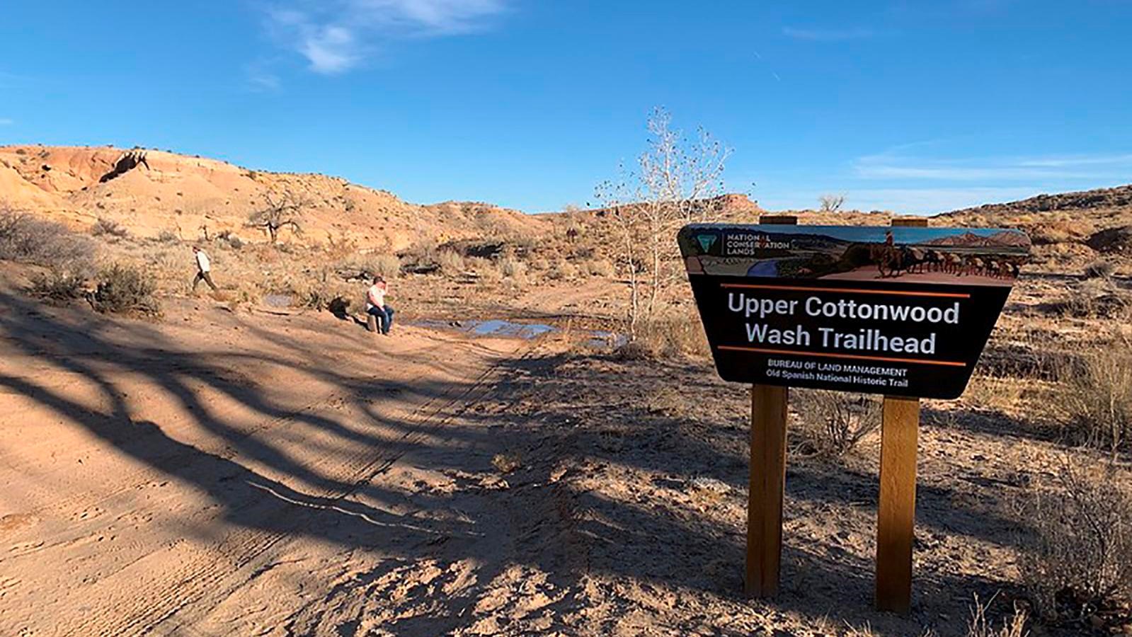 A open dirt area with a road and a trailhead sign. 