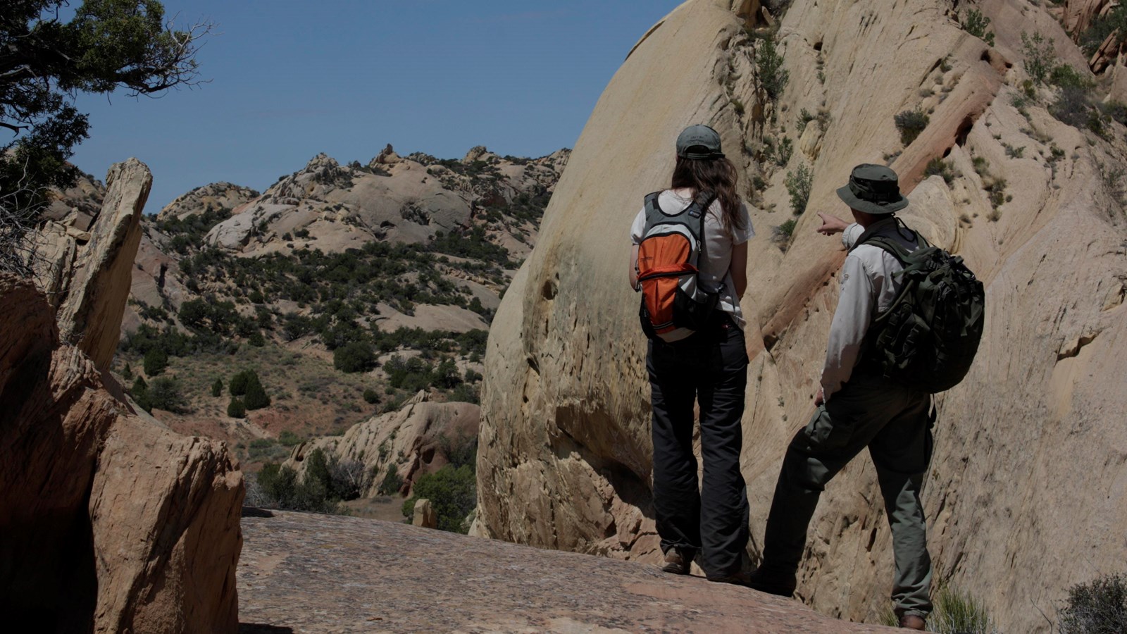 A pair of hikers in a sandstone clearing pointing off into the distance.