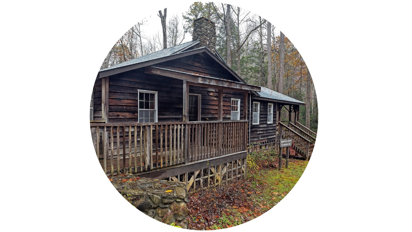 A rustic, brown cabin with two porches and a stone chimney. A forest surrounds the building.