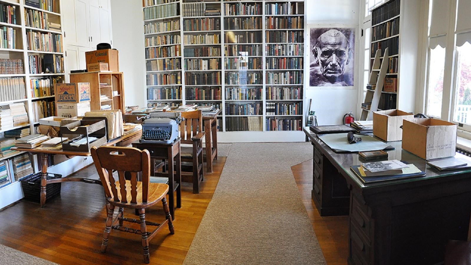Room filled with floor to ceiling books, desks stacked with books, and papers, vintage typewriter.