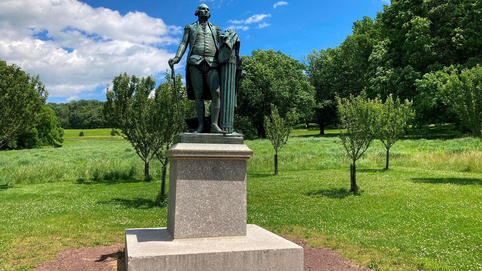 a bronze statue of a man standing with a cane sits on a granite pedestal