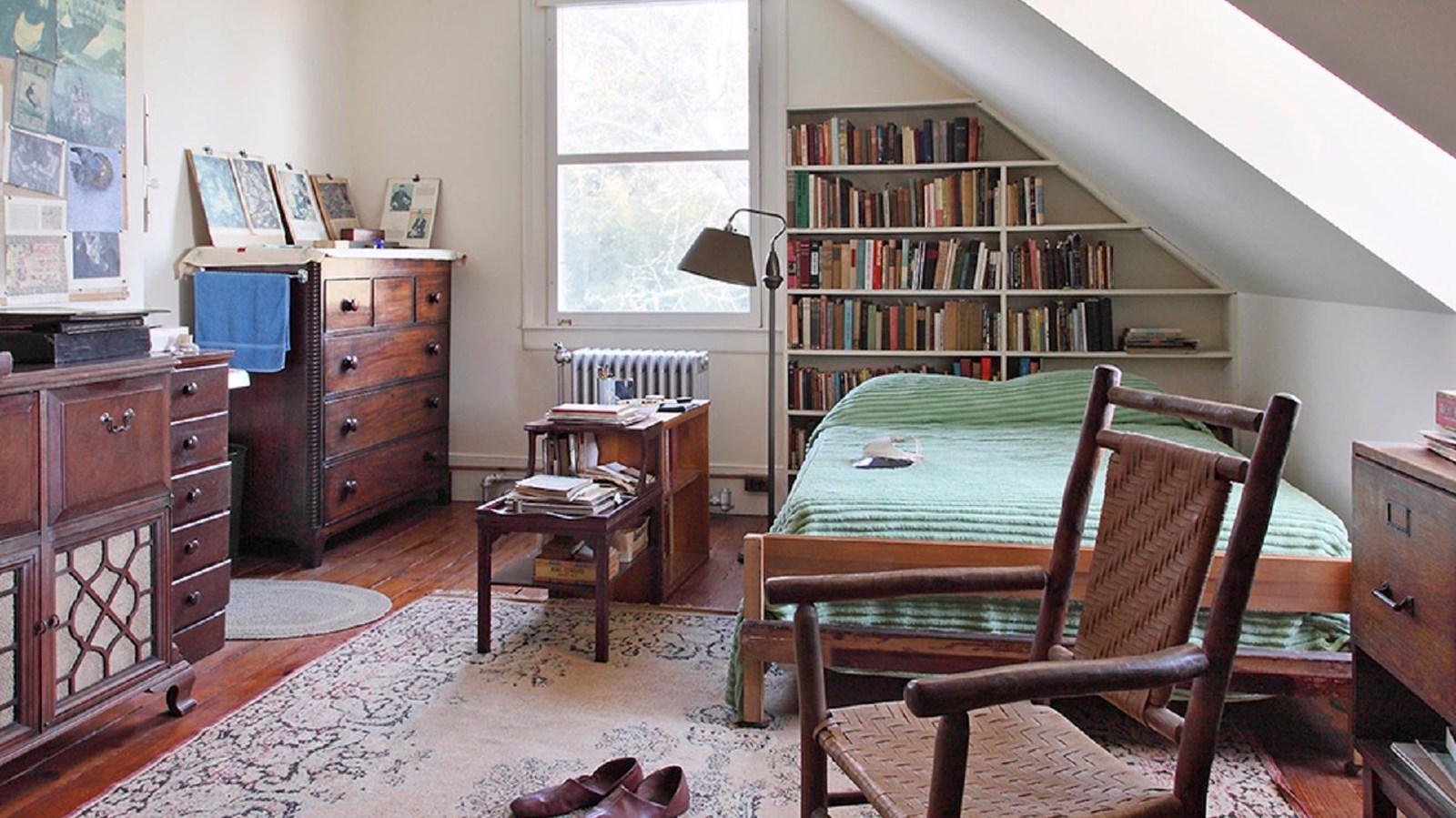 A bed, side table, dressers, wicker rocker, house slippers, and many books fill Carl\'s room. ks 