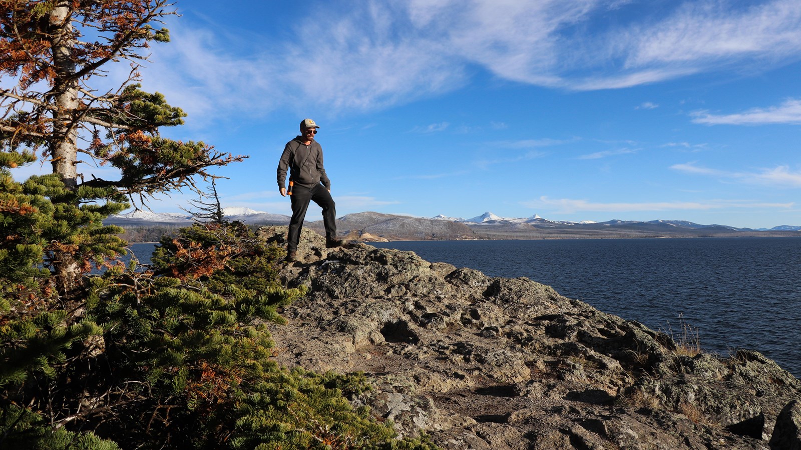 A hiker walks across a rocky outcropping above a large lake.