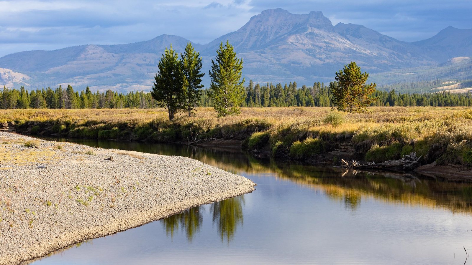 A calm creek meanders through a meadow with a mountain in the distance.