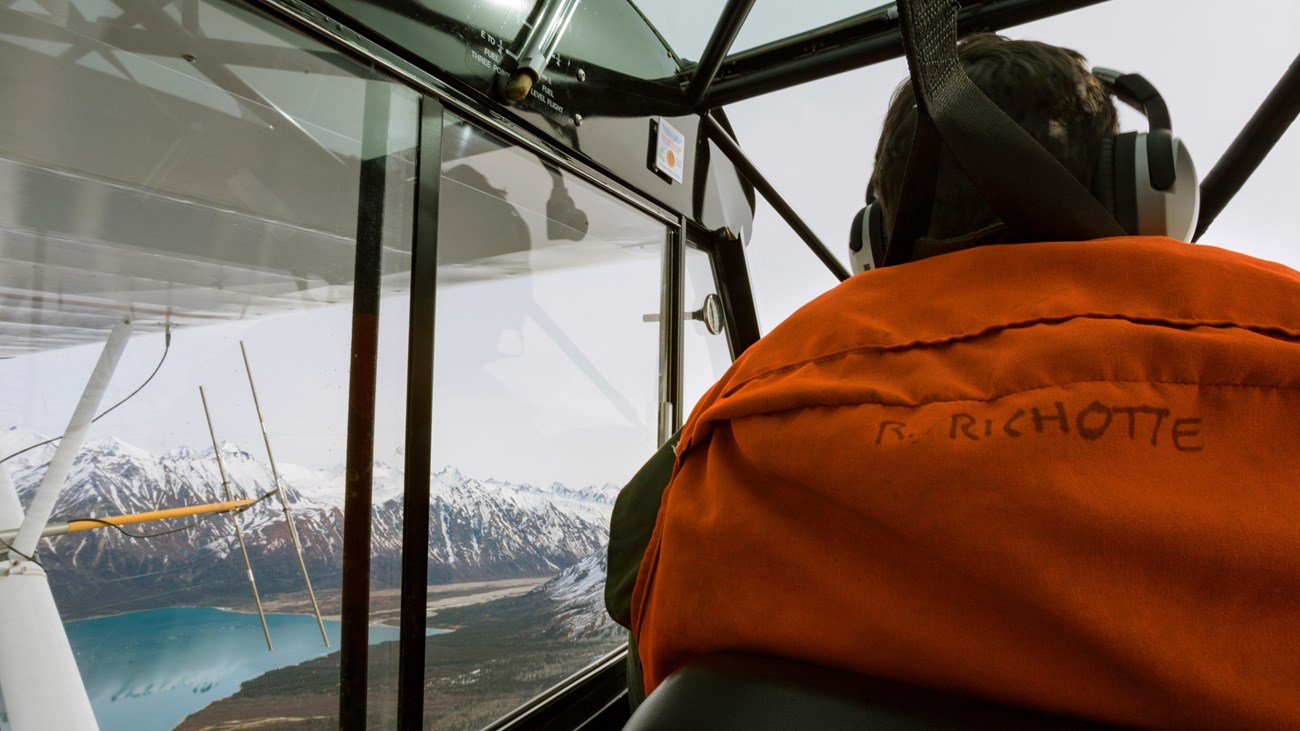 View of pilot inside a plane overlooking a mountain and a lake. 