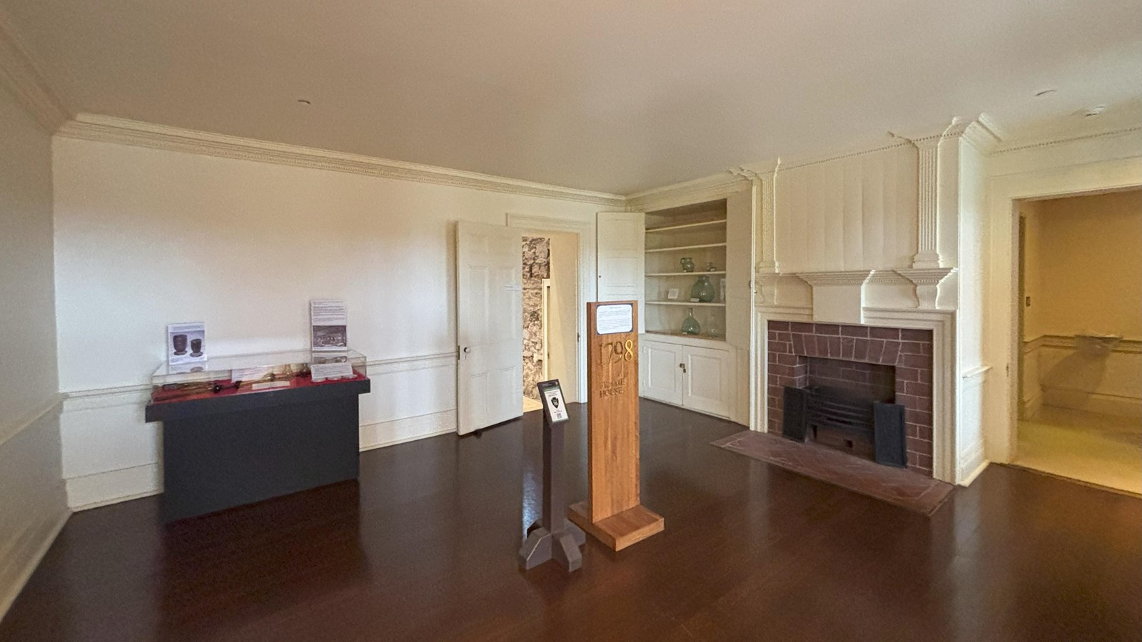 Square room with an exhibit case in the back left corner; a fireplace and built in exhibit on right
