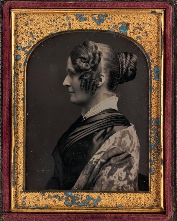 Daguerreotype of a side profile of a woman with curled hair and a high collared dress