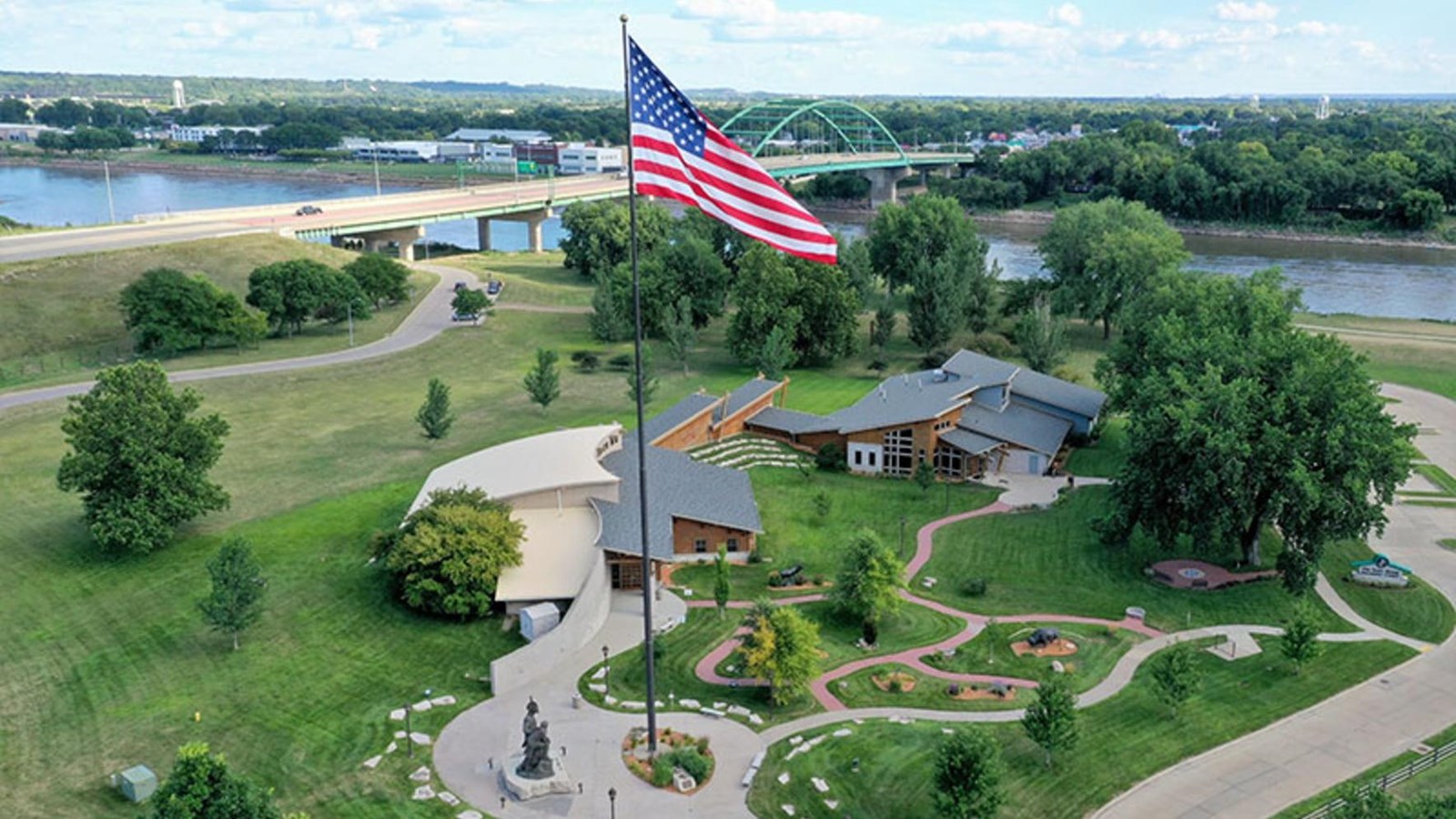 two modern buildings set in a park-like area, with walkways, a statue of Lewis and Clark, mature tre