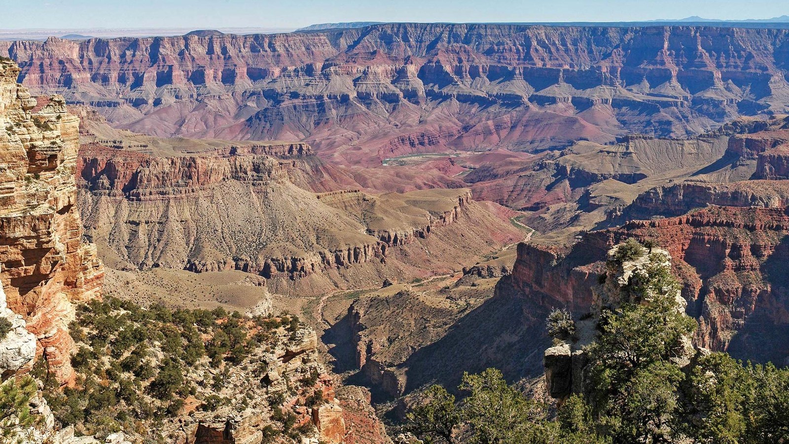Steep cliffs are shadowed to the right as multicolored horizontal layers make up the Grand Canyon.
