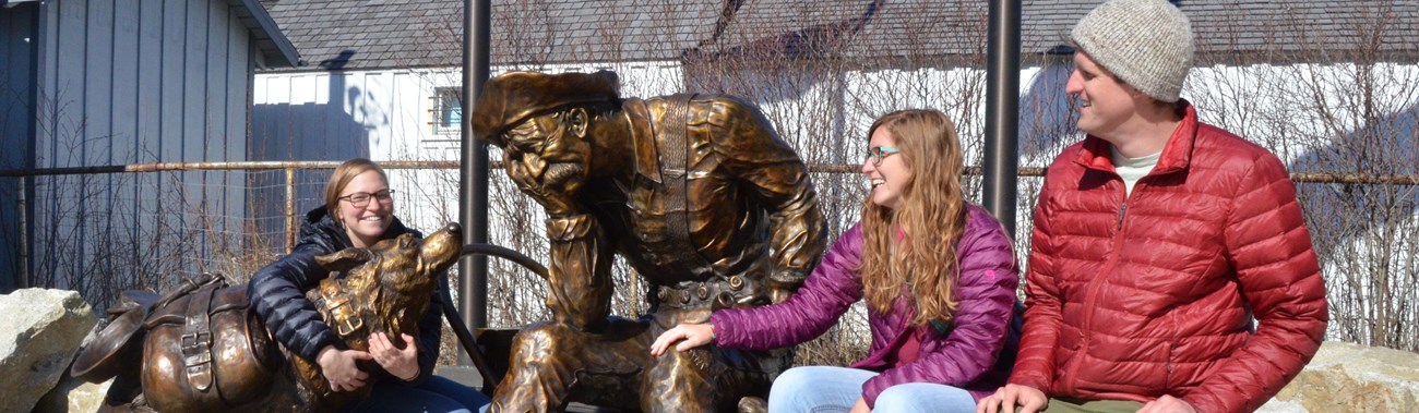 Three visitors sat next to a bronze statue of a gold prospector and his dog 