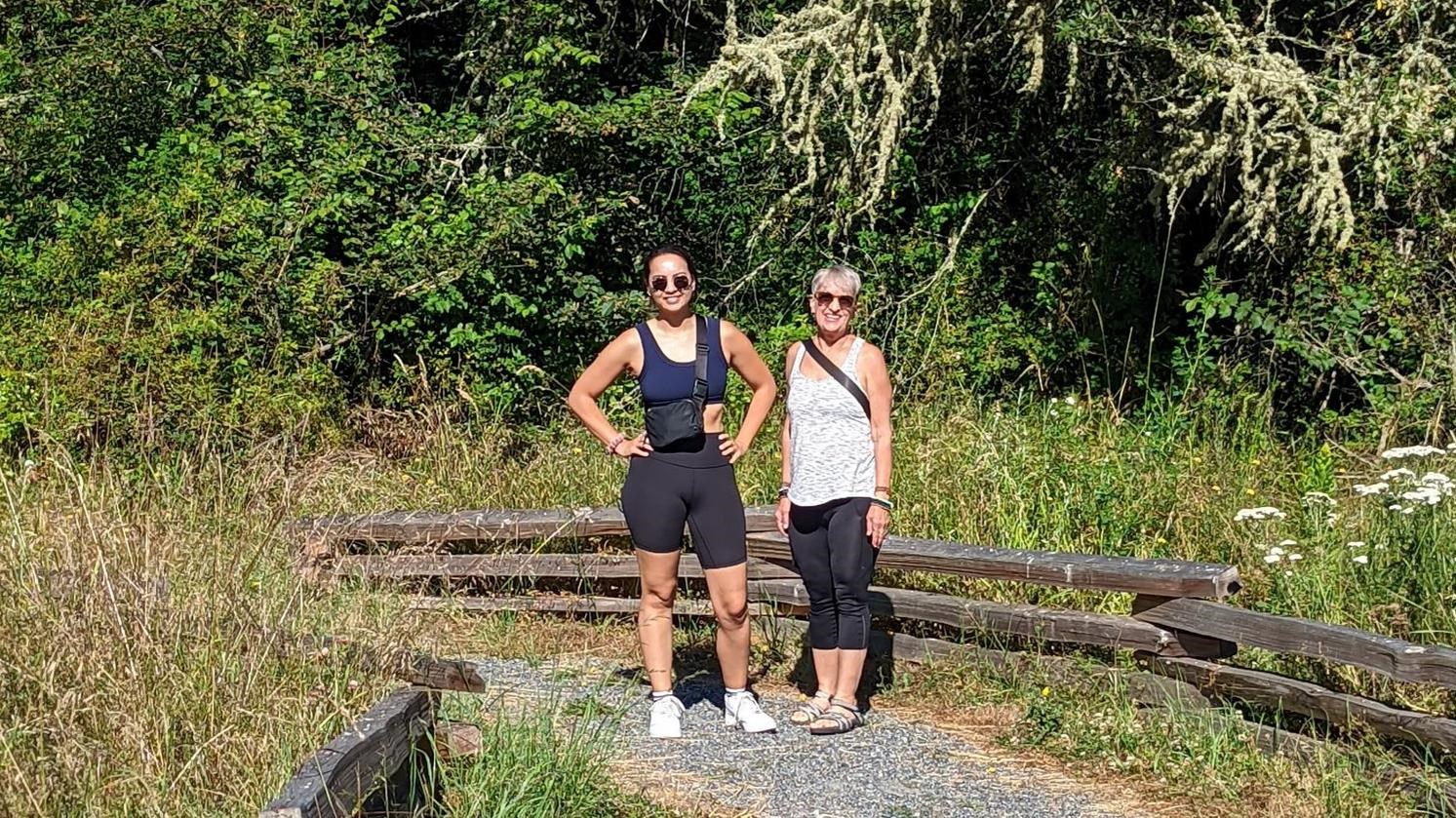 Color photograph of two women on a gravel path with trees behind them