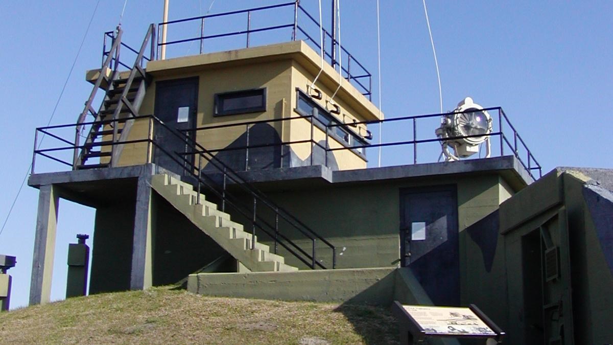 Concrete structure with signal flags flying. Grassy hill in foreground with a sign.