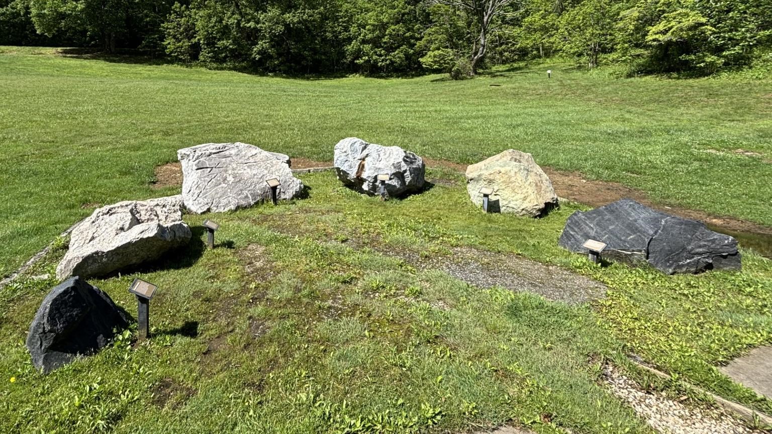 6 large boulders in semicircle with small plaques describing the type of rock each boulder is.