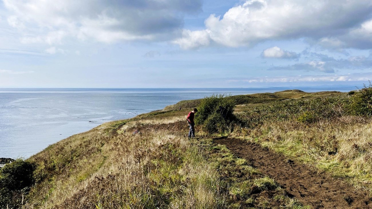 A hiker on a dirt trail along a hilly coastal bluff