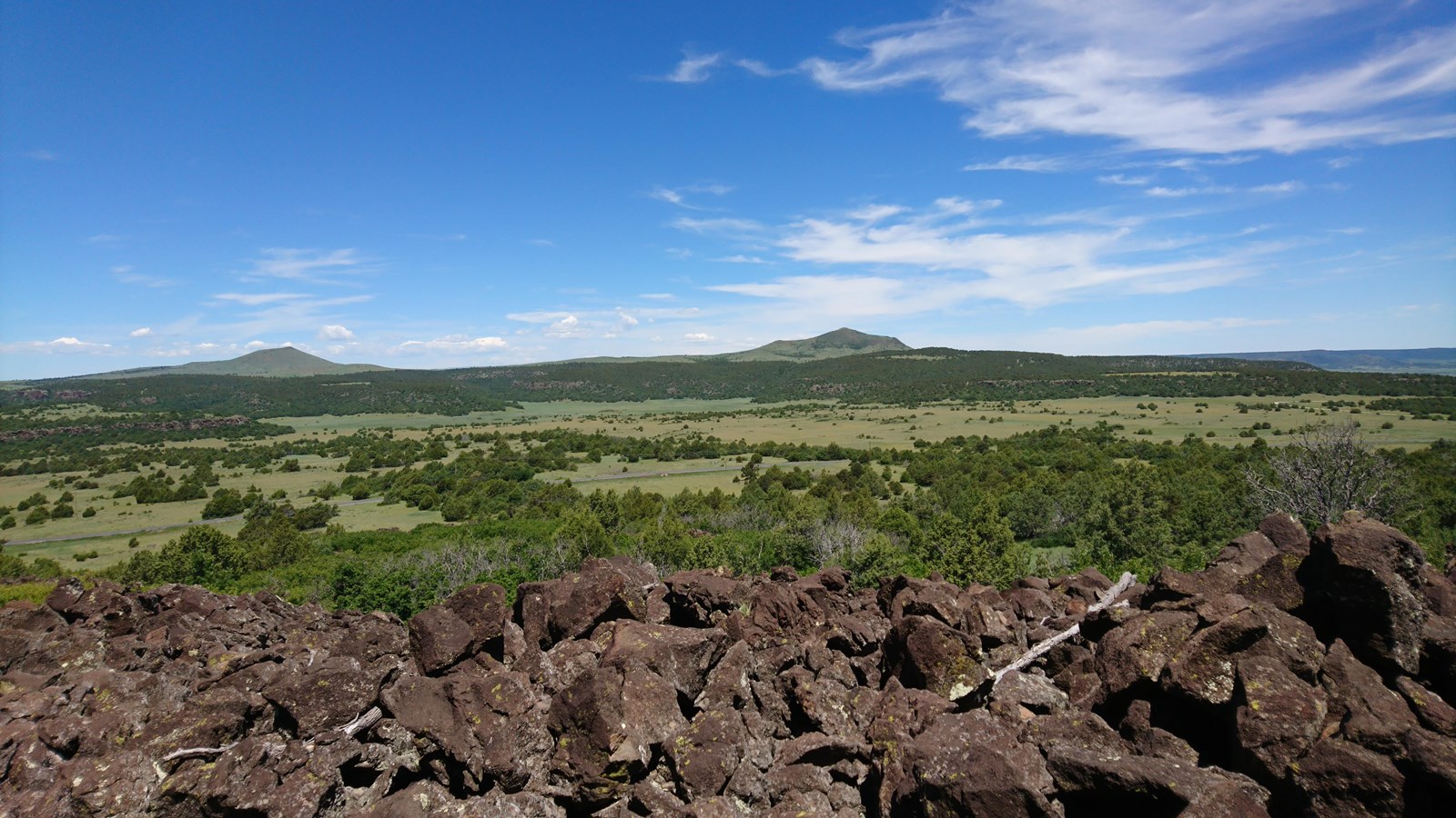 lava rock in the foreground and Jose Butte and Robinson Peak in the background under a blue sky