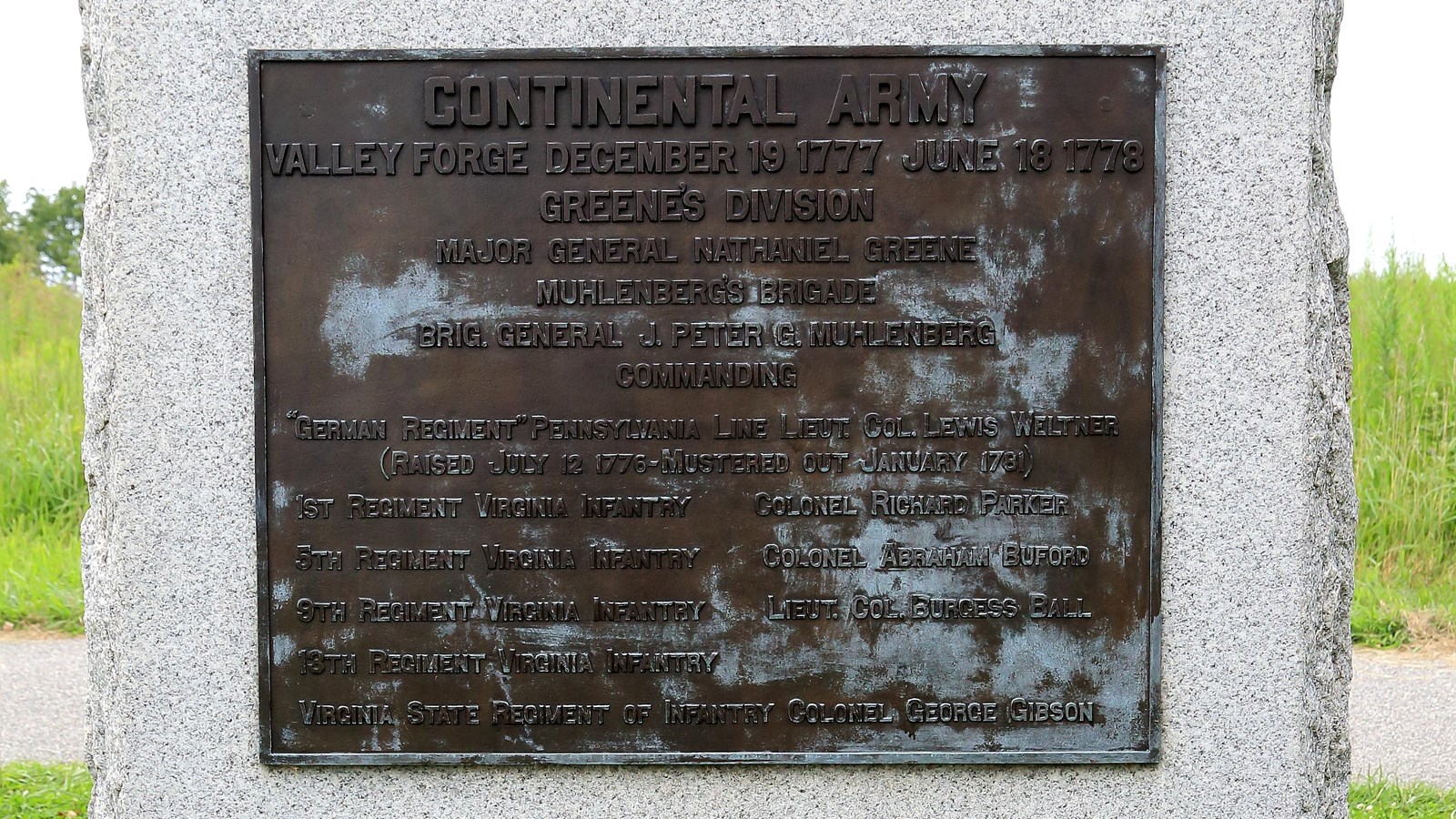 A large, smoothed granite block with a bronze plaque, sides and bottom rough.