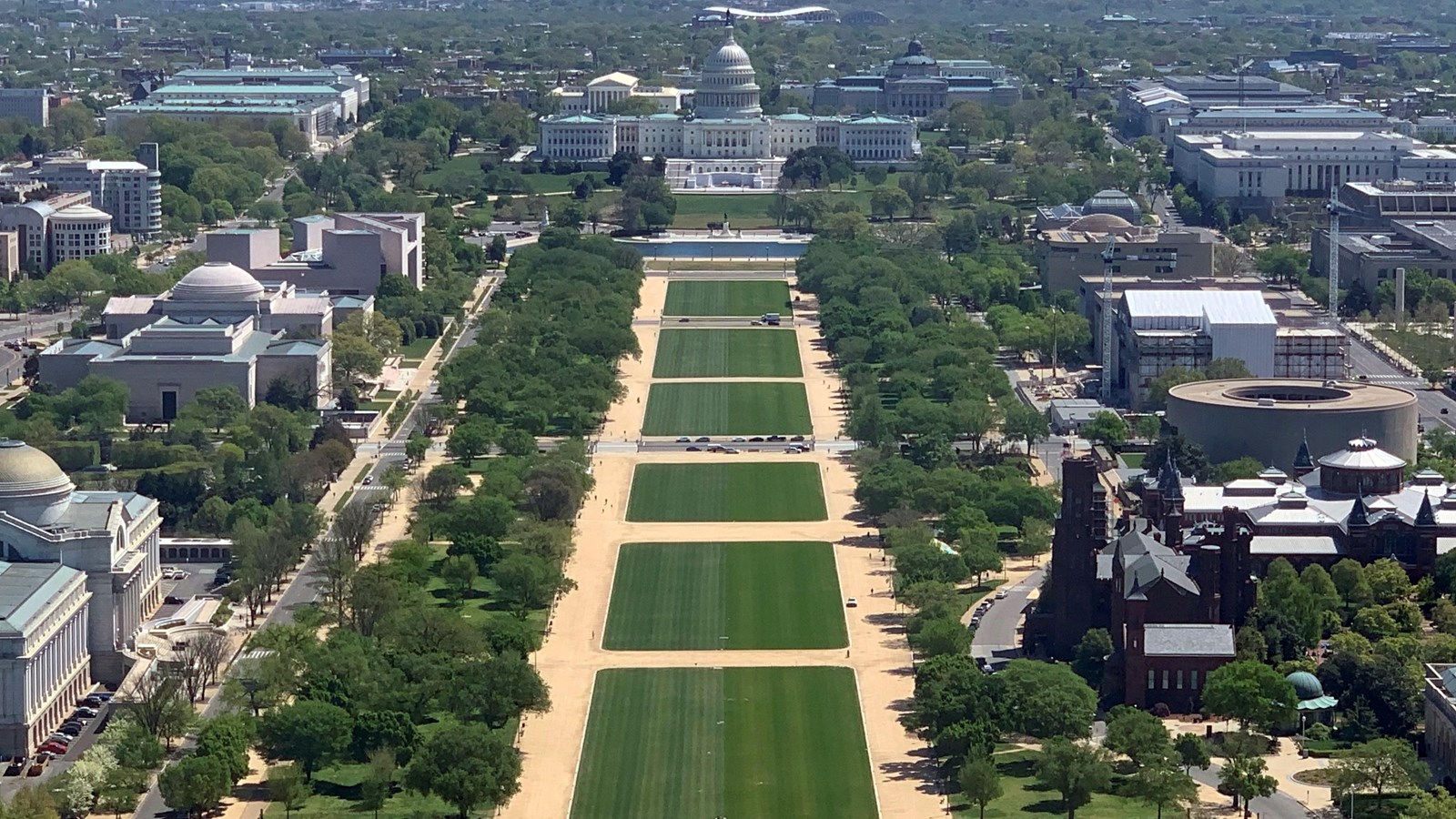 Large tree-lined grassy area with neo-classical buildings on either side and a domed building 