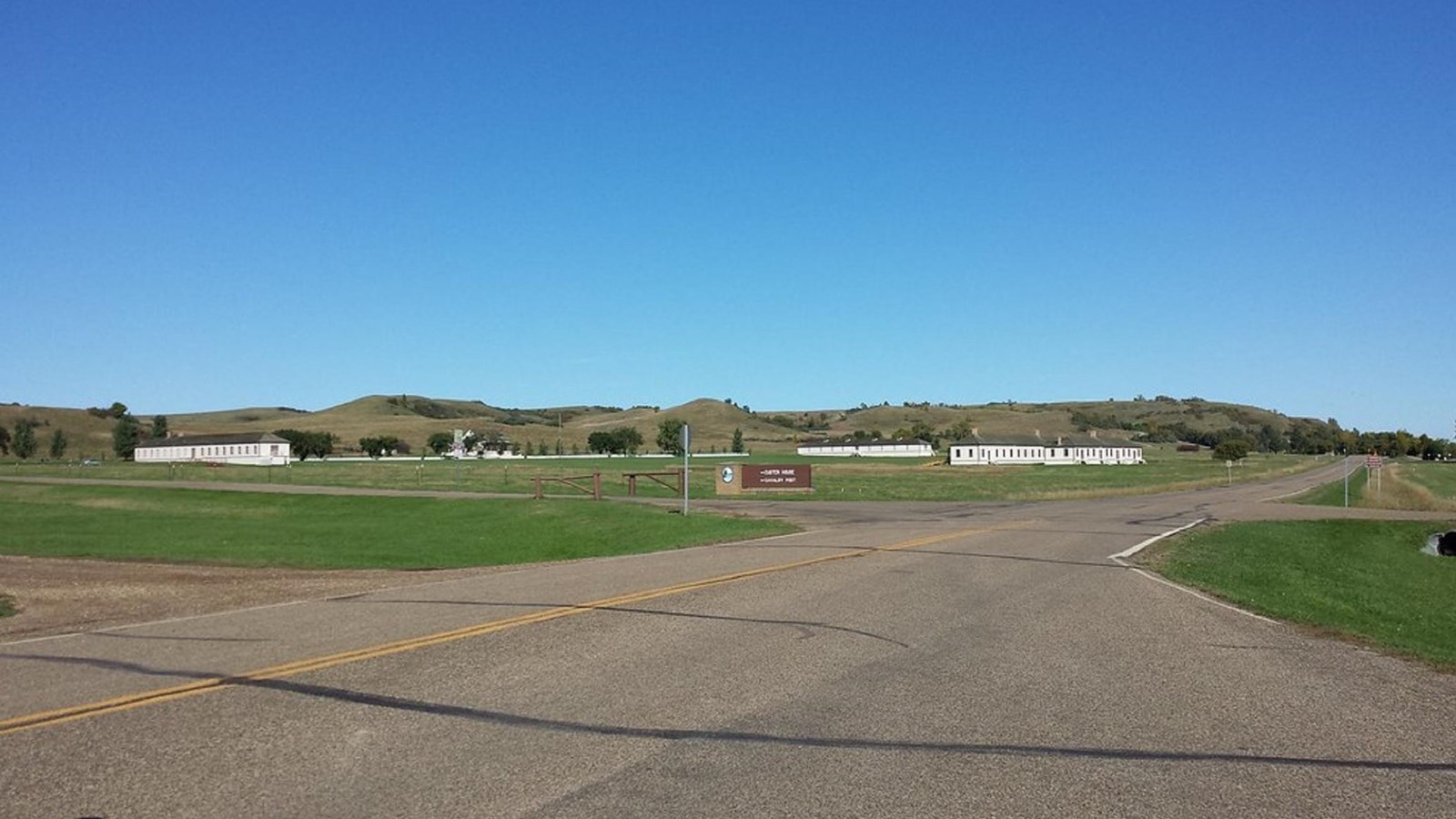 A paved road cuts through green lawn; white 18th century military buildings in the distance