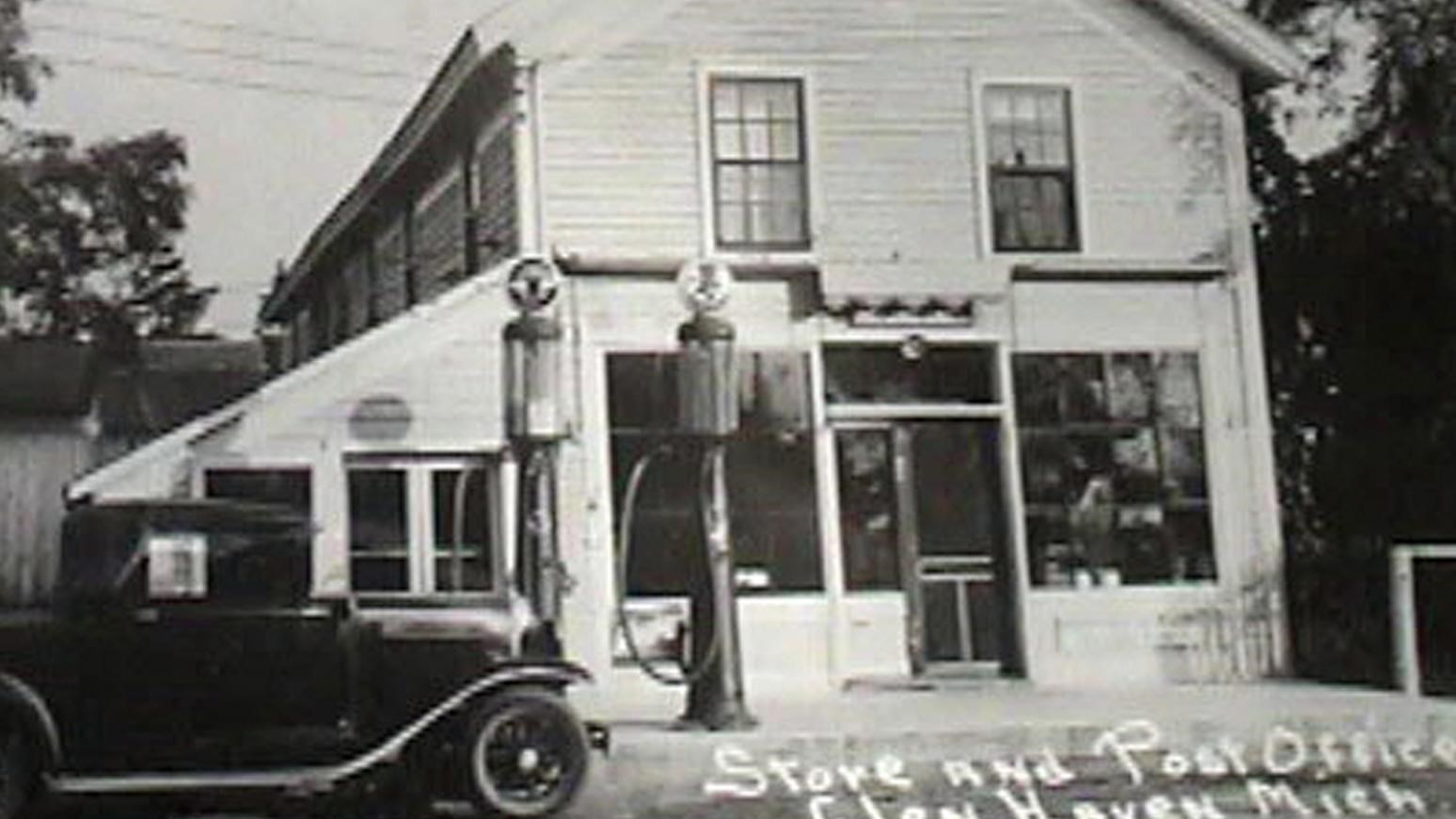 Historic photo of clapboarded building with two gas pumps and an early-1900s car parked in front