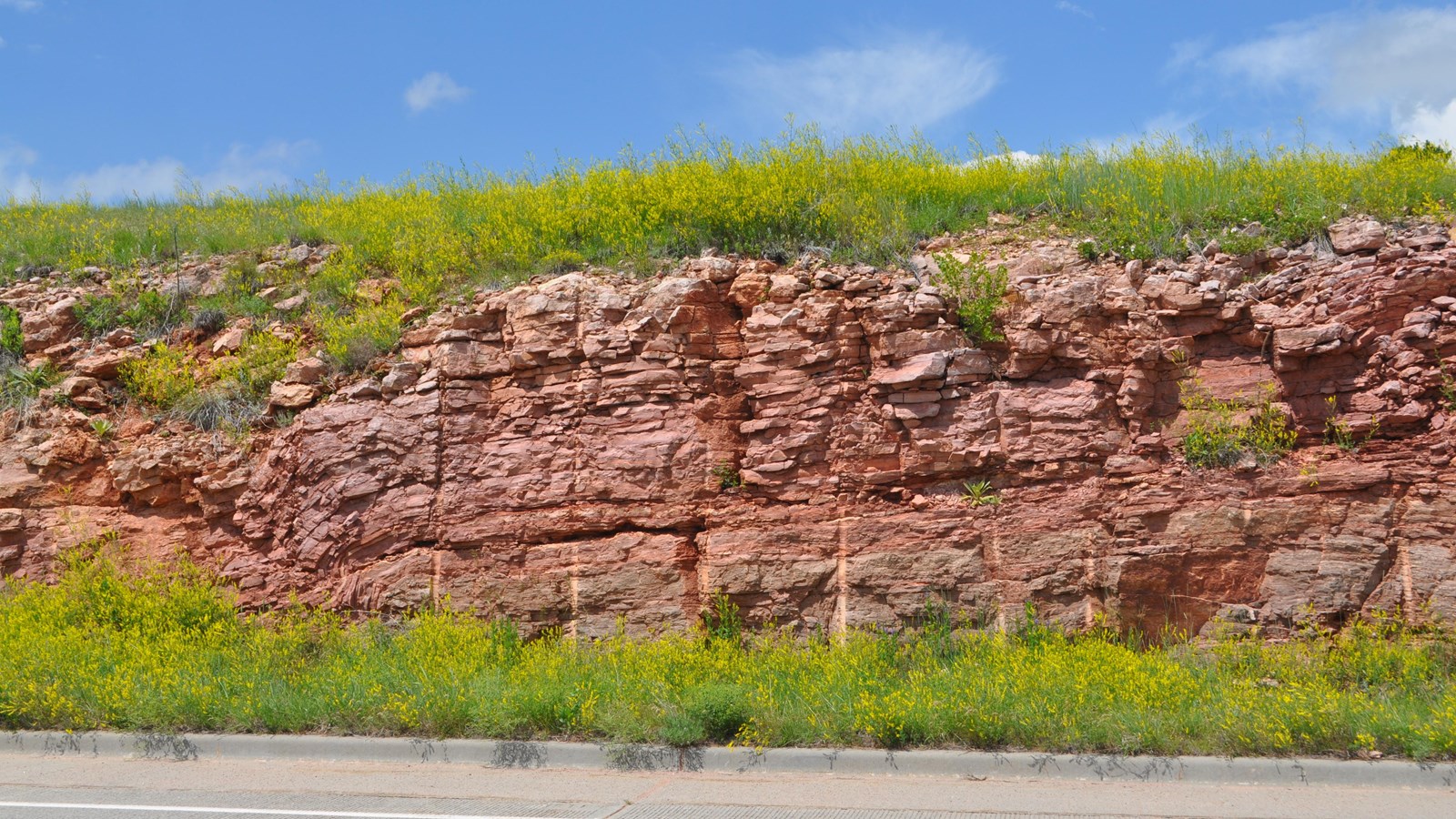 a layer of reddish stone made of many thinner layers next to a paved road