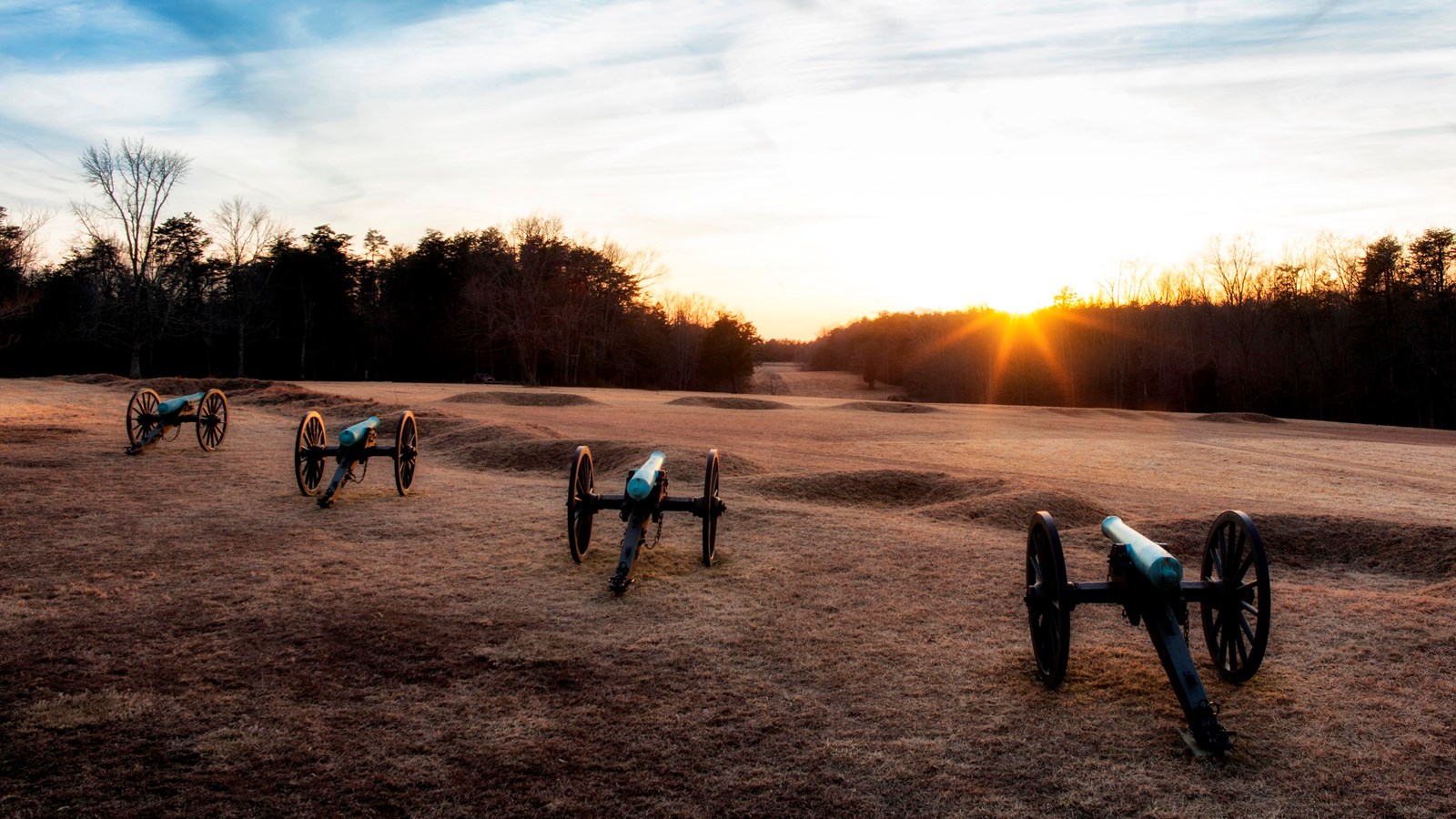 A line of cannons pointed across an open field at sunrise.