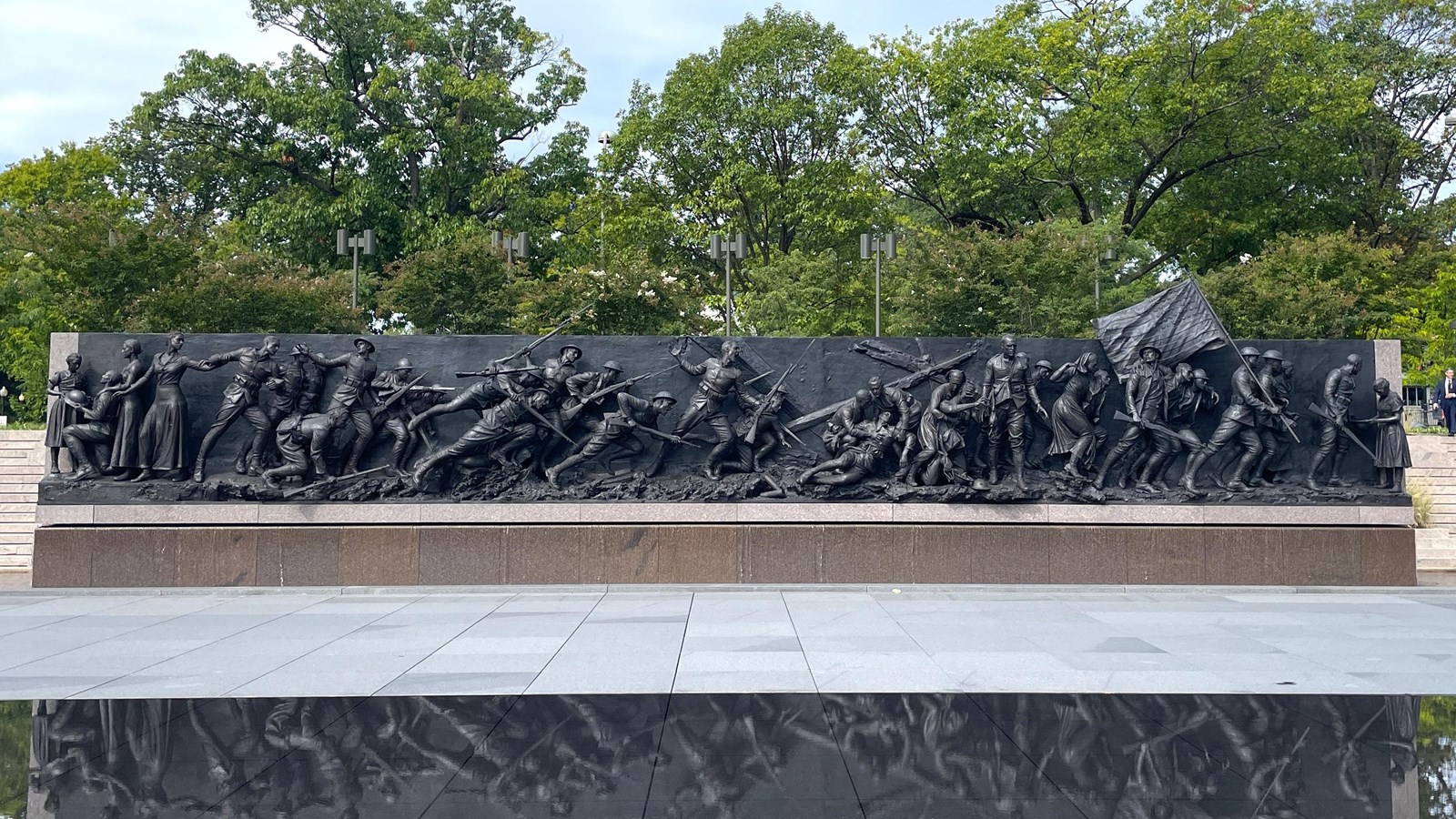 A rectangular pool in front of a stone wall with images of World War I soldiers.