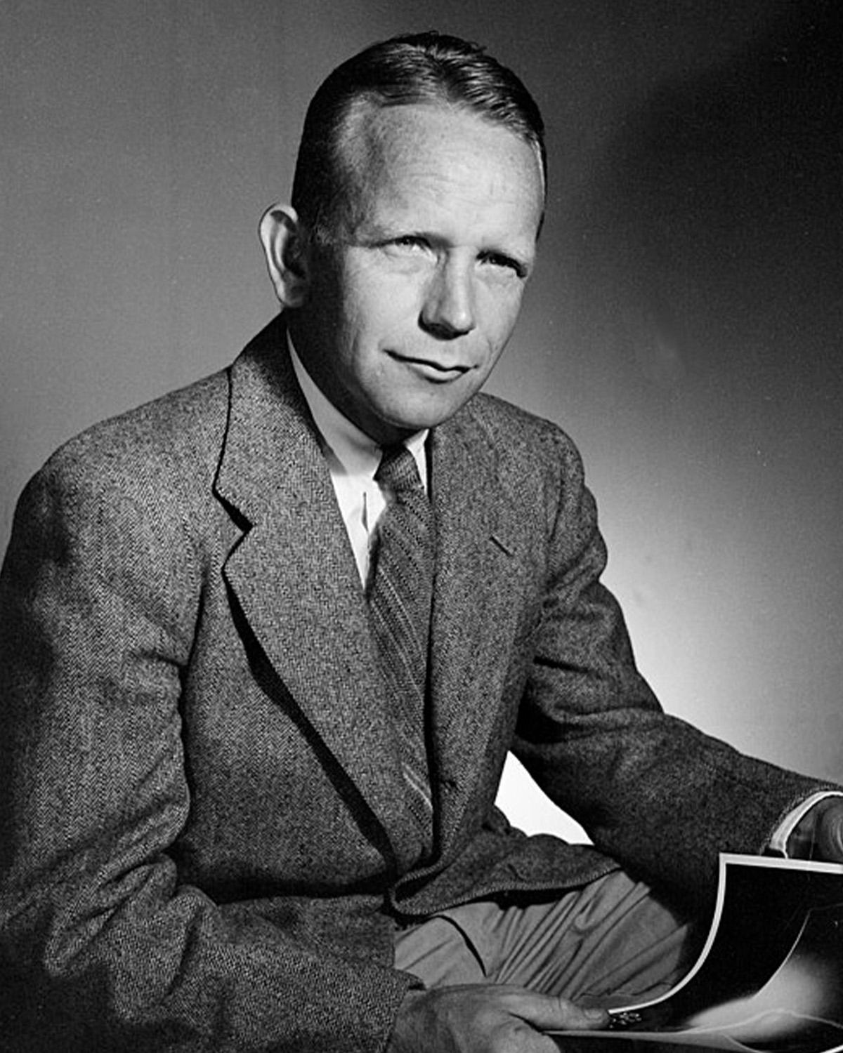 Black and white photo of a seated man in a suit, holding a photograph.