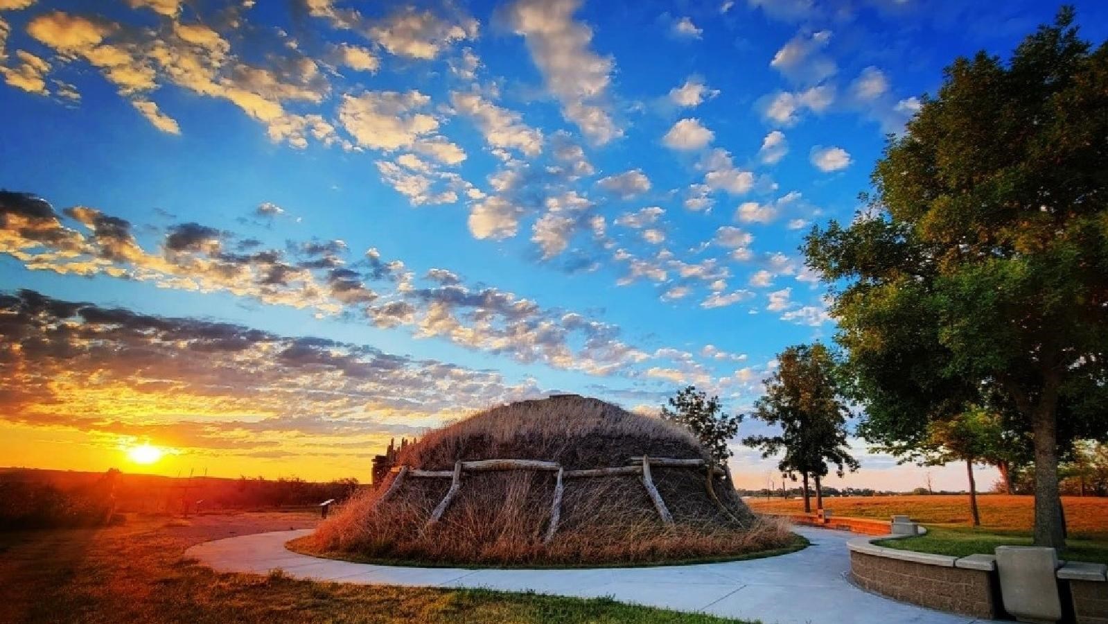 A brown, dome shaped lodge with a daisy chain of logs supporting sod covering on the sides and roof.