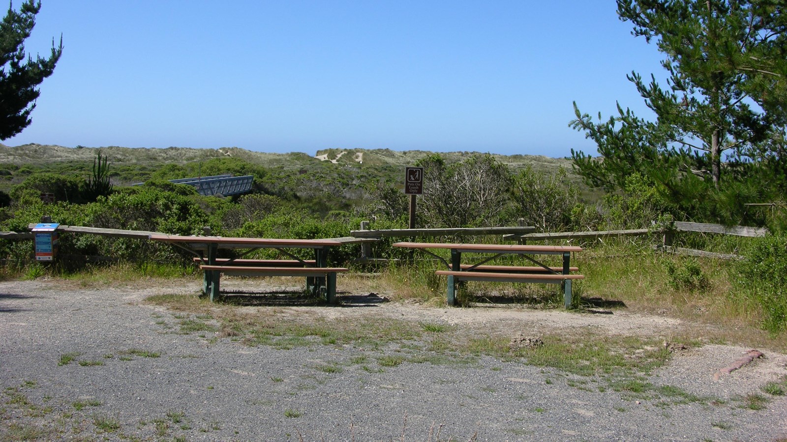 Two picnic tables adjacent to a split-rail fence with an estuary in the background.