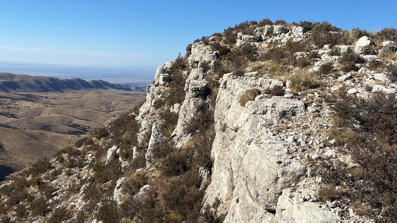 A desert mountain ends abruptly with a grey cliff