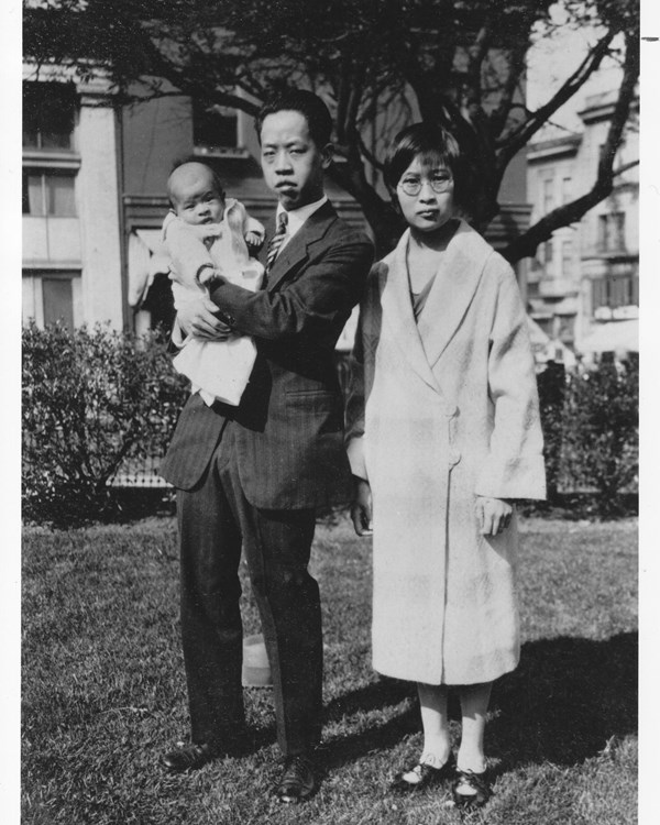 Black and white photo of an East Asian woman and man; the man is holding an infant.
