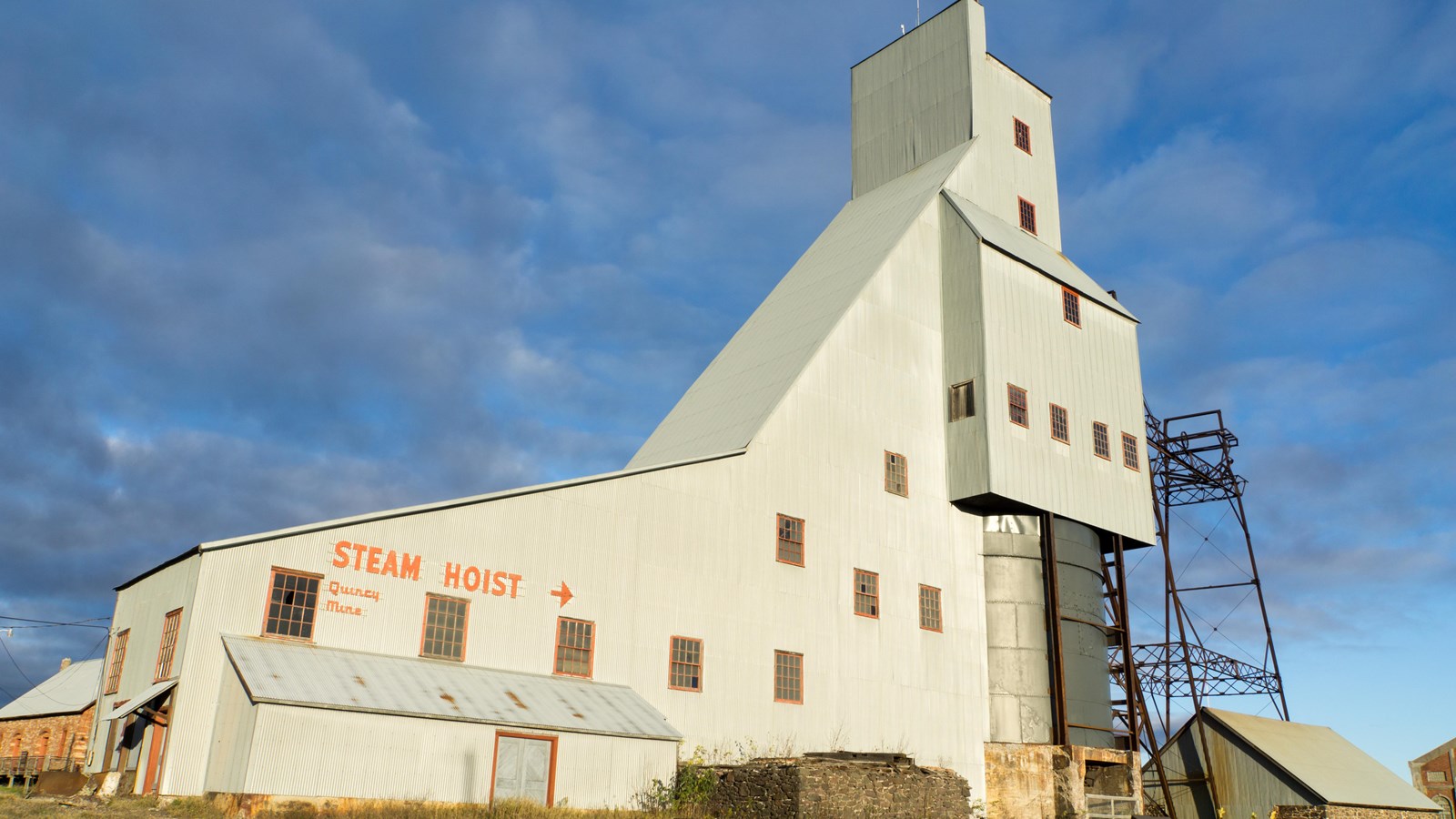 A 140 foot industrial building (shafthouse) lit by the setting sun with dark cloudy skies behind.