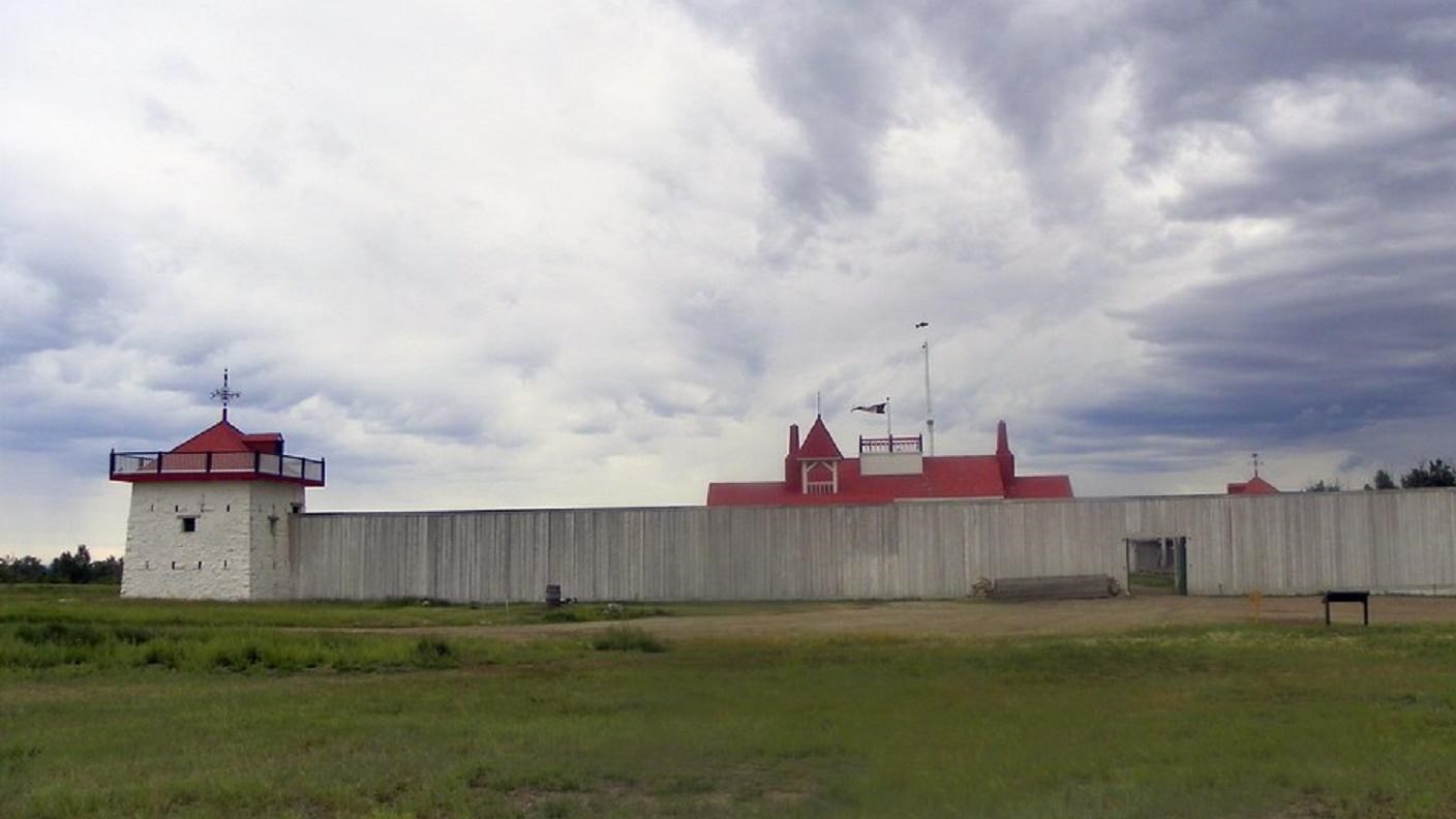 red-roofed building surrounded by white fencing, with a smaller building on the corner of the fence.