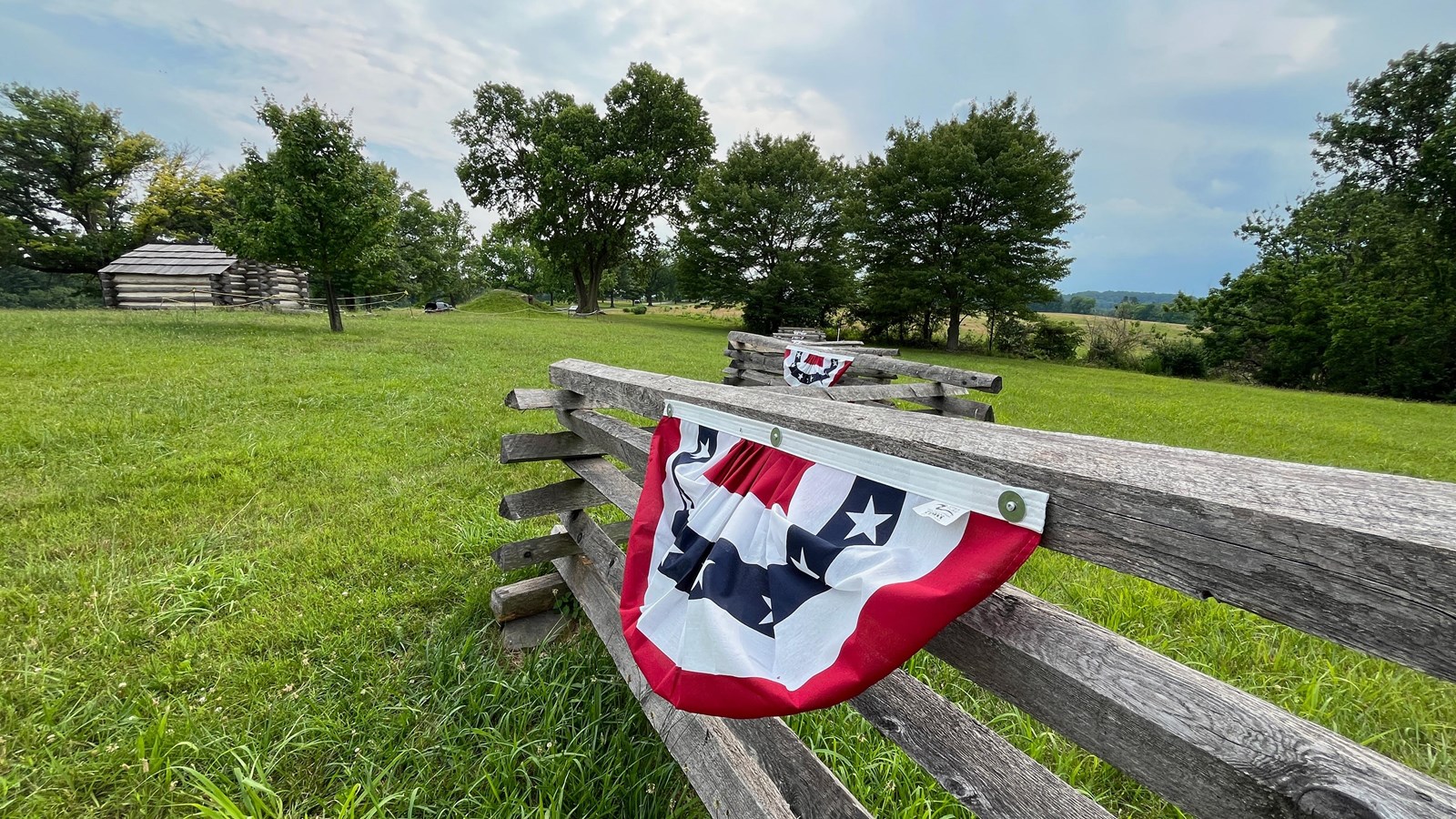 photo of wooden fence with red white and blue bunting. log hut in background