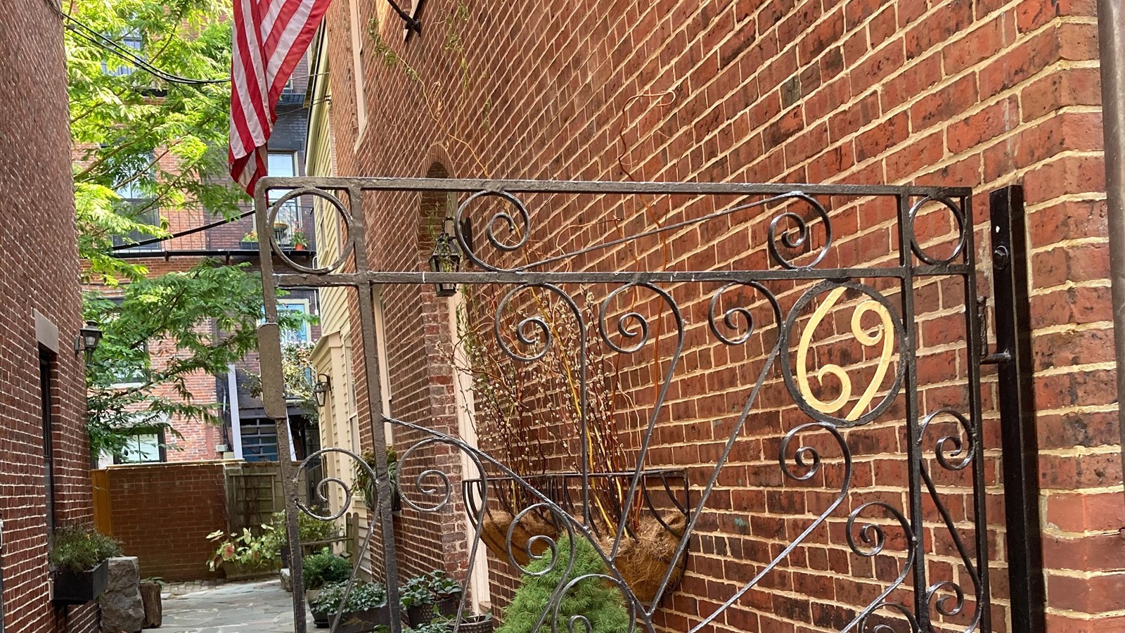 A metal gate in front of an alley way with the number 69 made out of metal on it. 