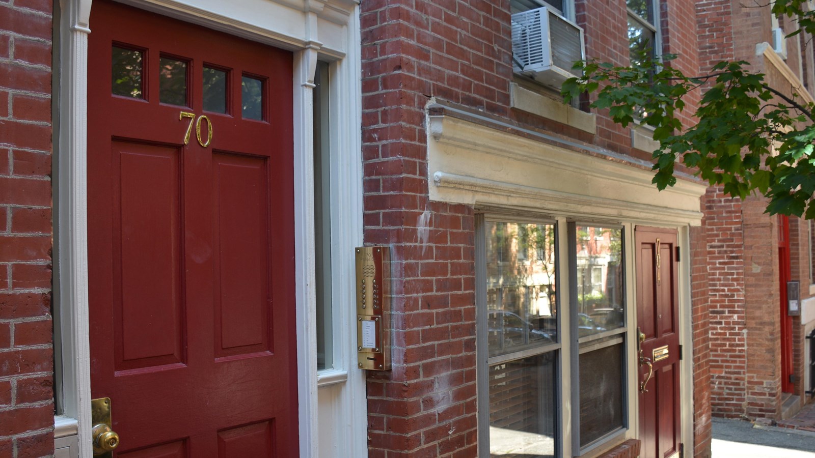 An angled view of a brownstone\'s entrance with a red door on the far left and far right. 