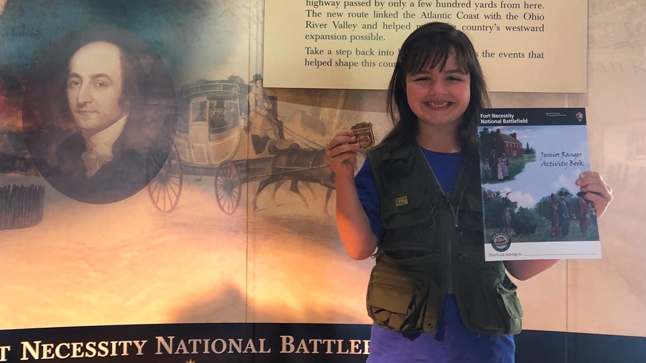 Girl holding a Fort Necessity Junior Ranger activity book and badge