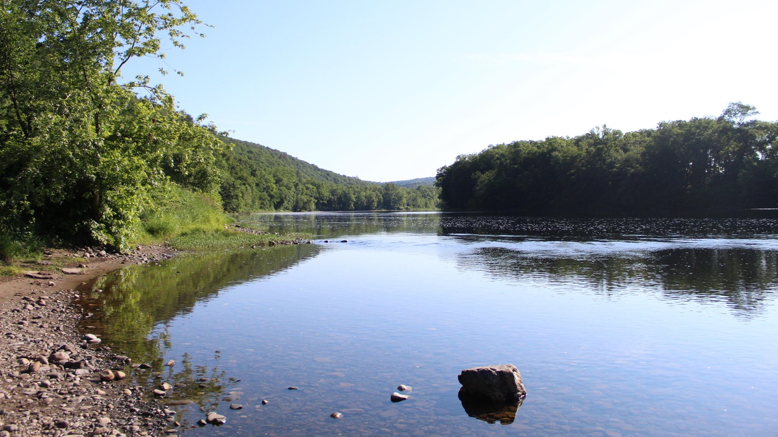 A rocky landing to the left slopes into the river, which is calm and glassy.