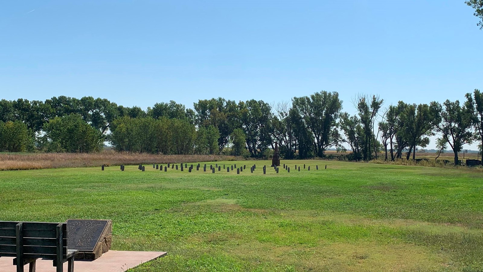 Far off view of wooden grave markers and a large pointed, stone monument.