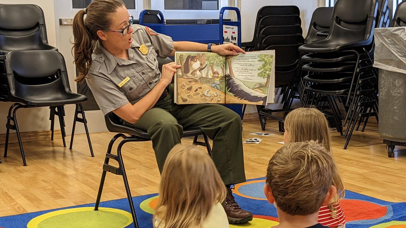 A park ranger reads a story book to several children. 