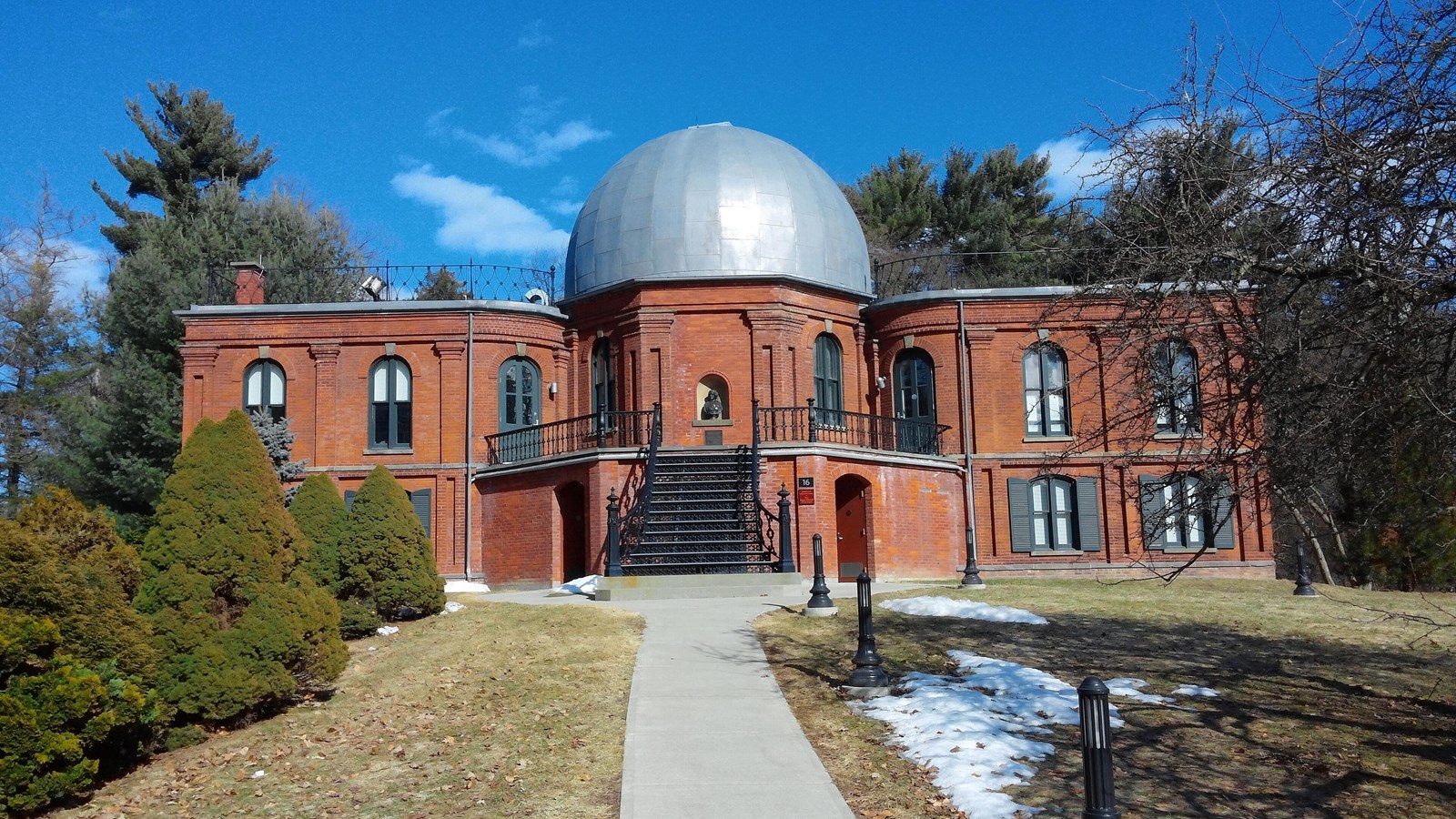A red brick observatory building with a large central dome, arched windows, and a stairway 