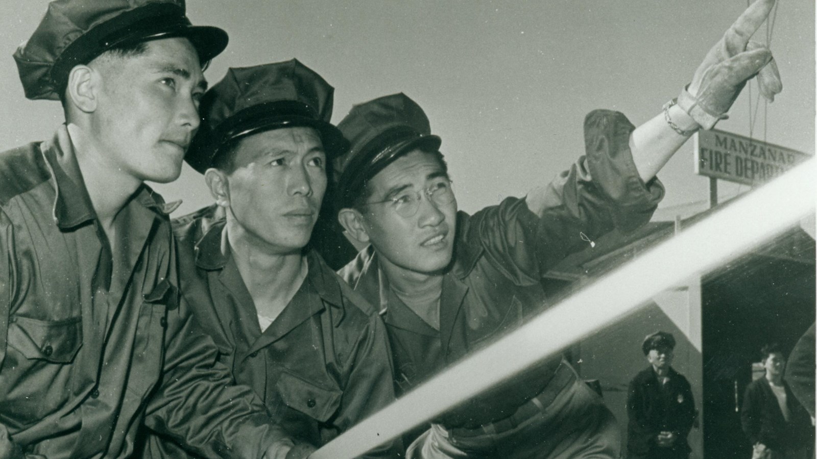 Black and white photo of three men holding a firehose