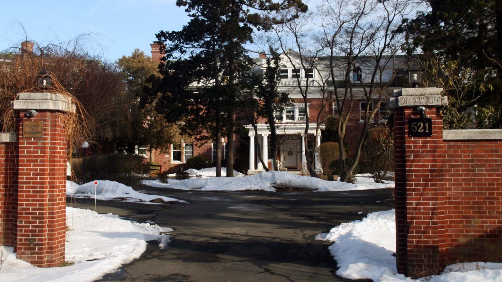 Brick building with white columns behind a gate and surrounded by piles of snow