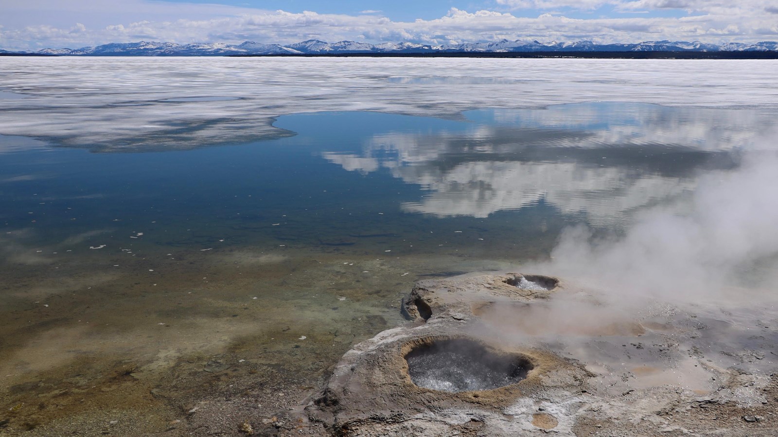 Water bubbles in a small geyser cone on the shore of a large, icy lake.