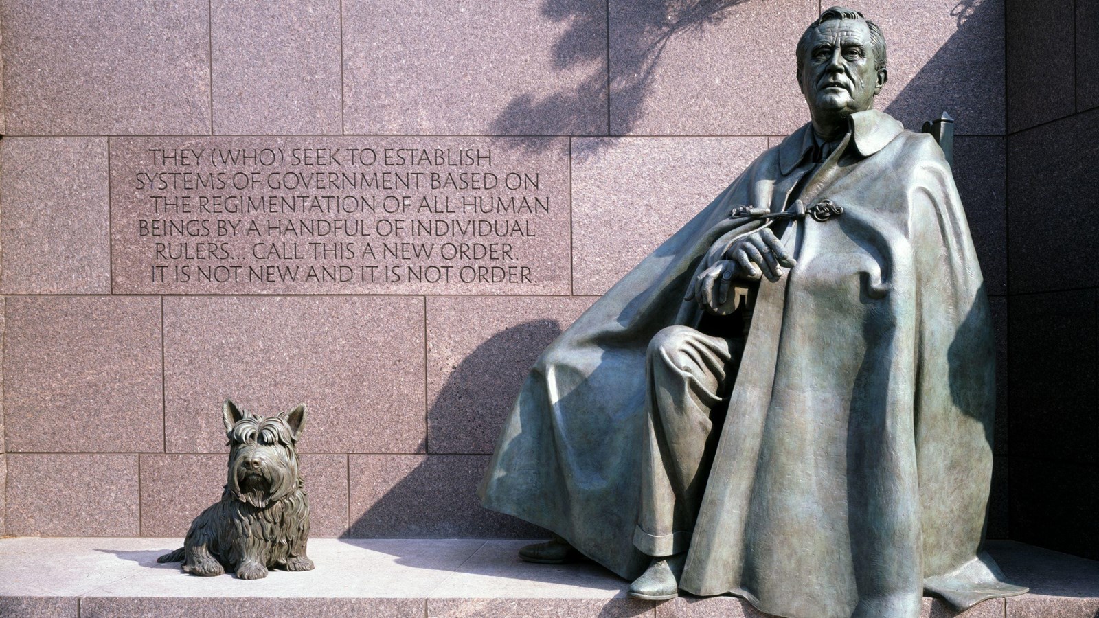 A bronze sculpture of seated Franklin Roosevelt with a cloak obscuring his chair, with his dog Fala.