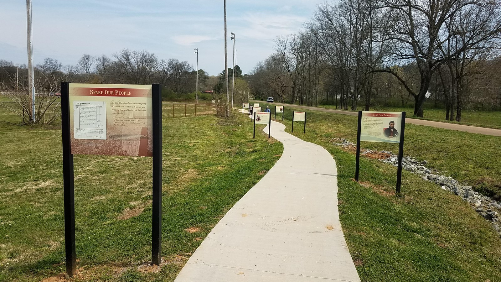 A path winds through a grassy field, lined by large, upright interpretive exhibits.