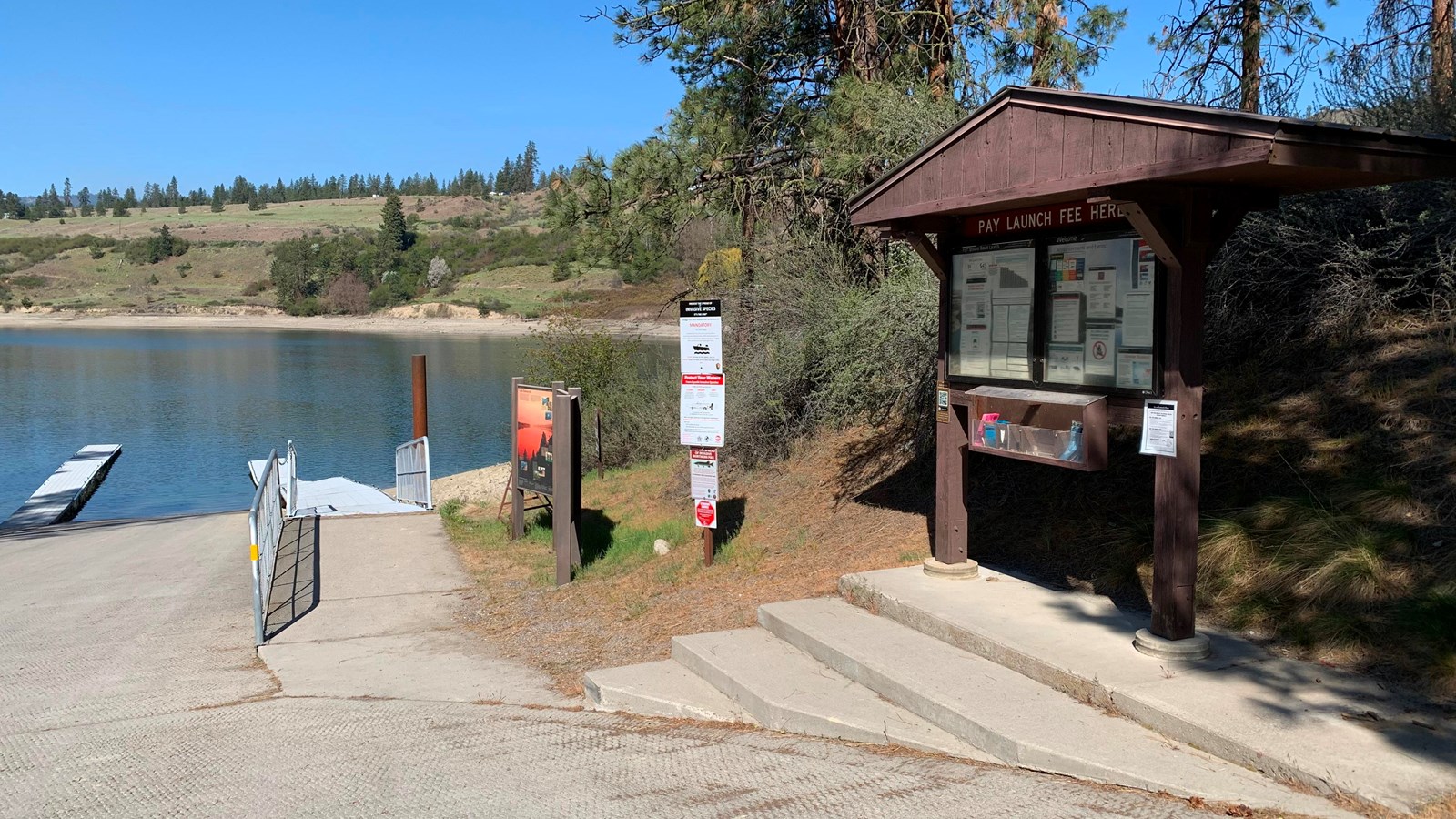 The information kiosk stands to the right of the boat launch, the lake and far shore are visible.